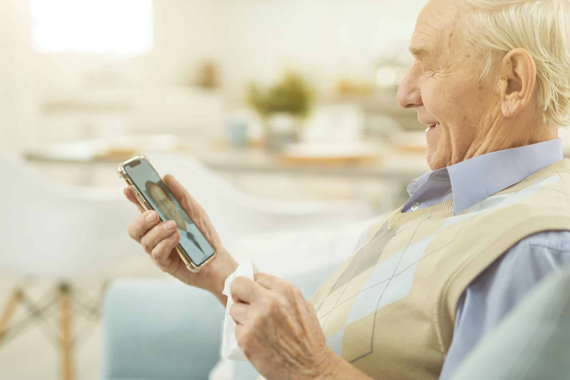 Uomo anziano sorridente che guarda lo smartphone e chatta online con un medico