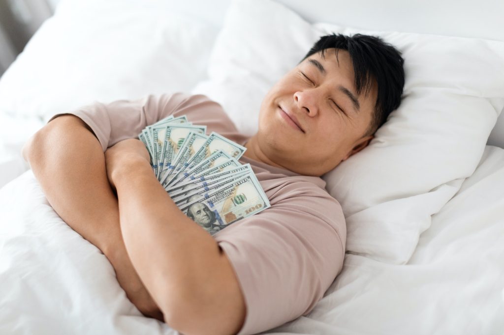 Uomo cinese addormentato felice che abbraccia mazzo di contanti