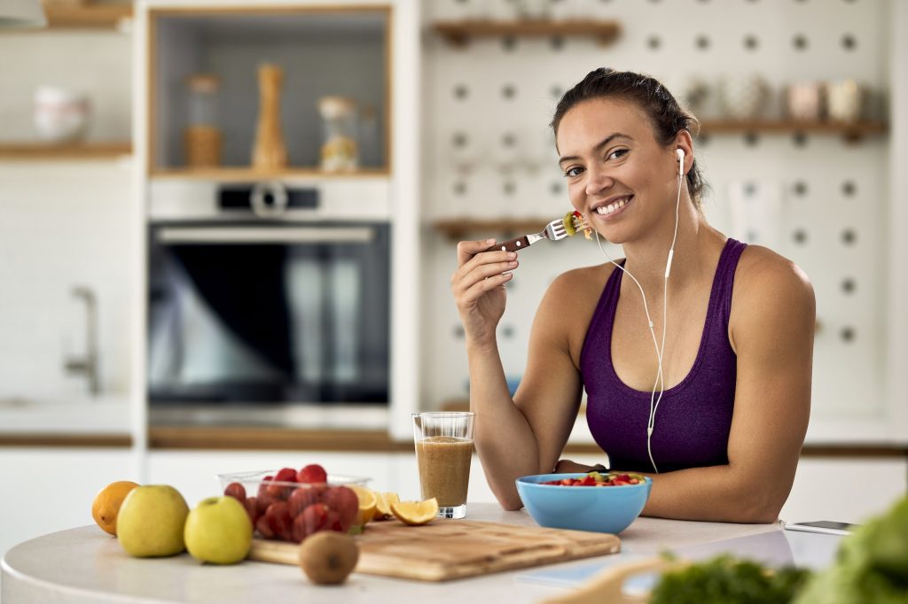 Giovane donna atletica felice che mangia insalata di frutta in cucina.